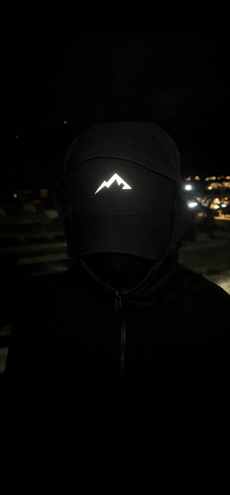 A hooded figure at night. The Alpinix three-peak mark glows on the cap front.